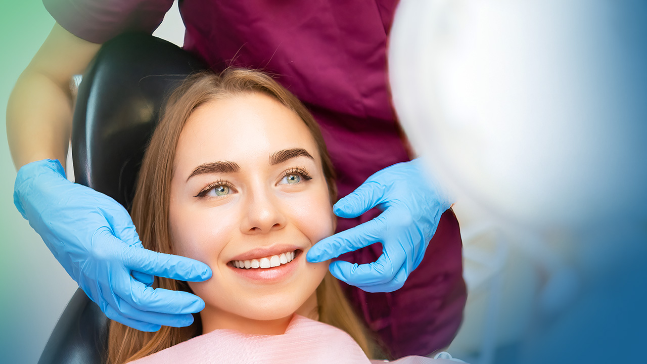 Woman in dental chair looking at new smile in a hand mirror